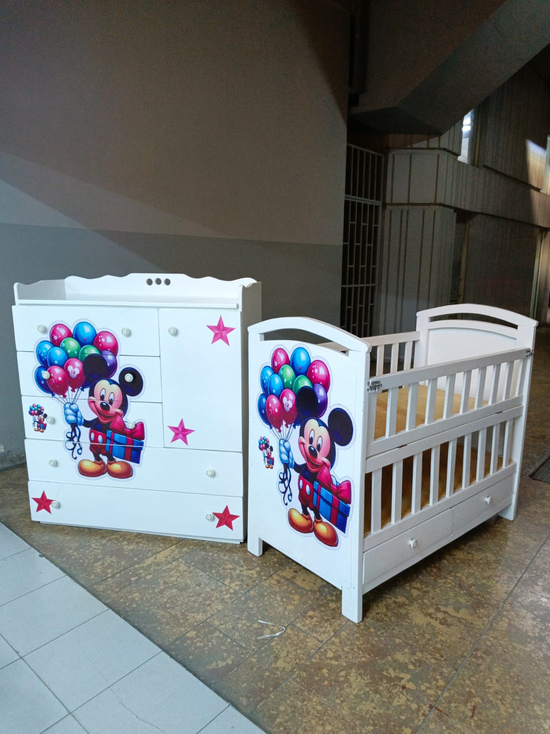2 x 4 Feet Mickey Mouse-themed wooden baby cot and a matching 4 x 4 Feet chest of drawers.